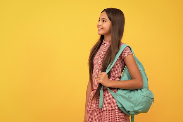 Happy school kid carry backpack on yellow background copy space education