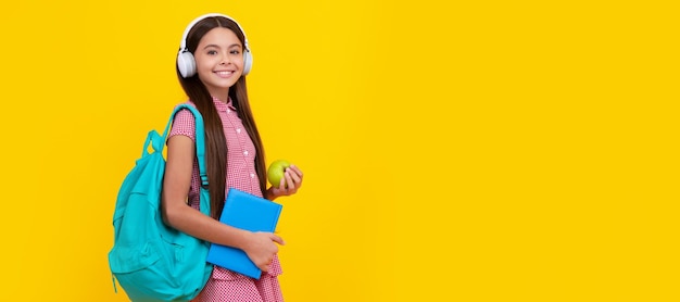 Happy school kid in headphones carry backpack and workbook with apple for lunch healthy lifestyle banner of school girl student schoolgirl pupil portrait with copy space