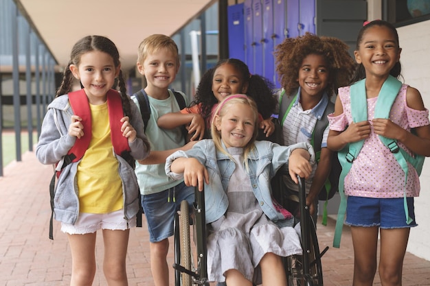 写真 女子高生が車椅子に座っている間、廊下に立つ幸せな学校の子供たち