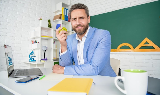 Photo happy school teacher in classroom having lunch break with apple