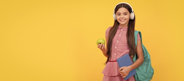 Happy school teen girl in headphones carry backpack and workbook with apple for lunch Banner of schoolgirl student School child pupil portrait with copy space