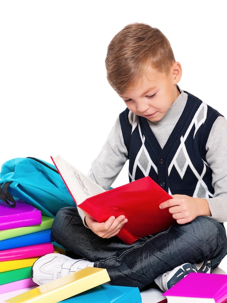 Happy schoolboy sitting on floor with books on white background
