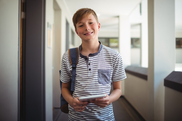 Happy schoolboy using digital tablet in corridor at school