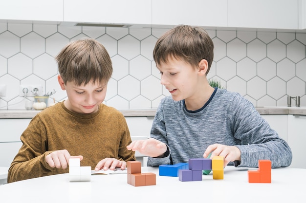 幸せな男子生徒は、テーブルに座っておもちゃのコンストラクターを再生します。子供たちは、レゴ フォールド テトリス フィギュアの色の詳細を収集します。