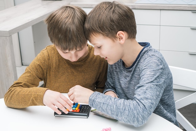 Happy schoolboys play toy constructor sitting at table Children collect colored details on playing board Board games