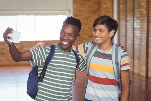 Happy schoolboys taking selfie on mobile phone in campus