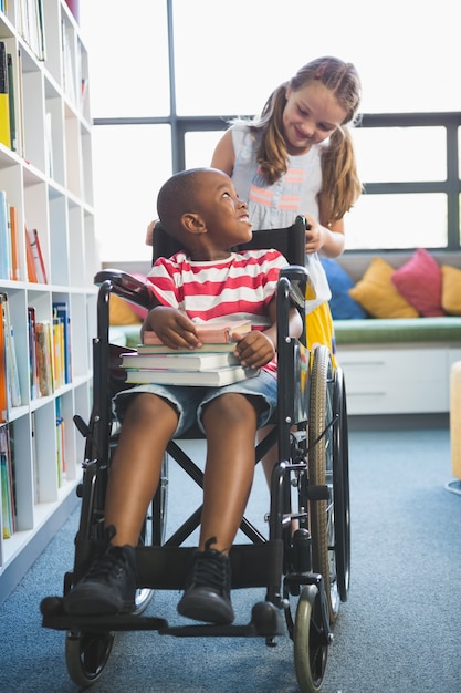 Happy schoolgirl carrying schoolboy in wheelchair