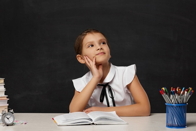 Happy schoolgirl daydreaming and sitting at table