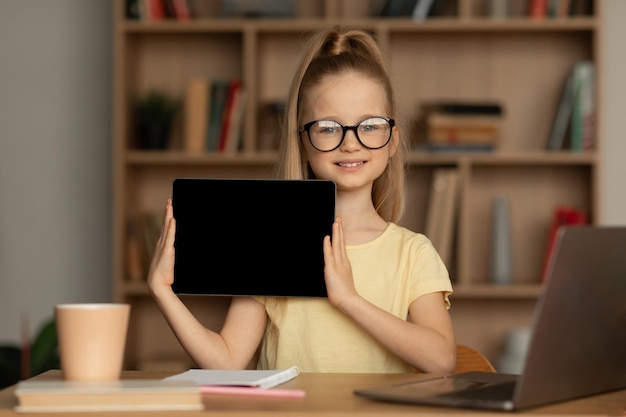 집에서 빈 화면으로 디지털 태블릿을 보여주는 행복한 여학생