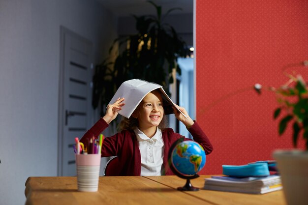 Happy schoolgirl smart girl arms put workbook on the head