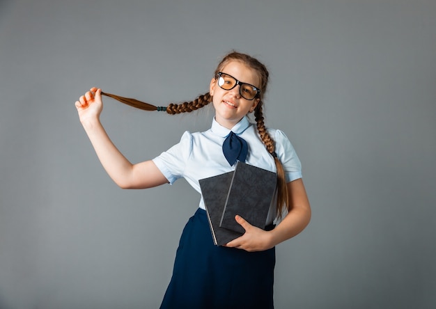 Happy schoolgirl standing with book in hands, isolated on gray background