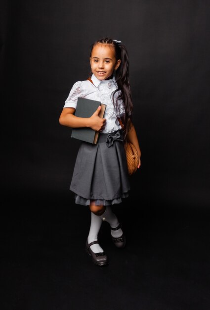 Happy schoolgirl standing with a book in her hands, isolated on dark background.