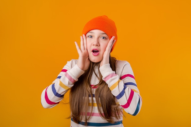 Happy schoolgirl with long hair holds her hands in front on a yellow background