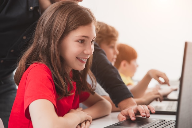 Happy schoolgirl with teacher using laptop during lesson