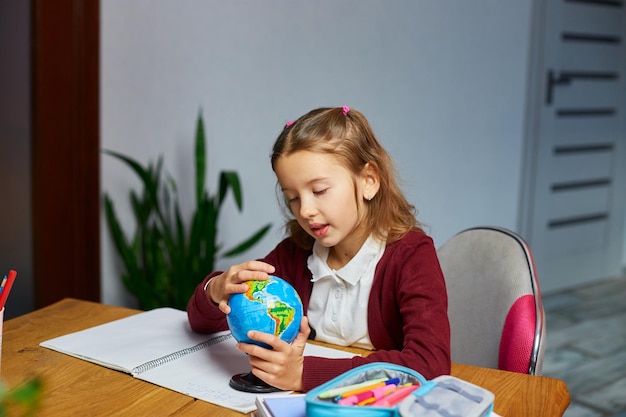 Happy schoolgirl at workplace studying globe in classroom