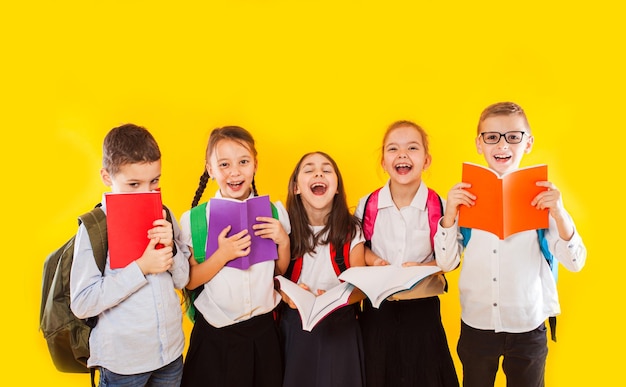 Happy schoolkids standing with colorful books isolated on yellow background kids hiding face behind books