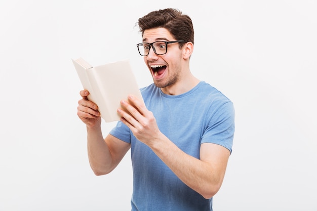 Happy screaming nerd in eyeglasses and t-shirt reading book over grey wall