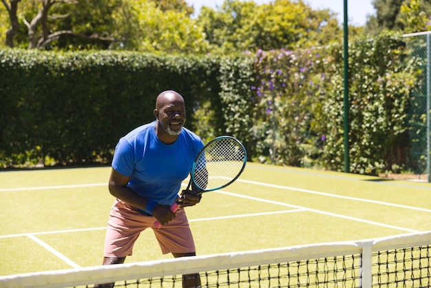 화창한 잔디 코트에서 테니스를 치는 행복한 아프리카계 미국인 남자. 시니어 라이프 스타일, 은퇴, 스포츠, 여름, 피트니스, 취미 및 여가 활동.