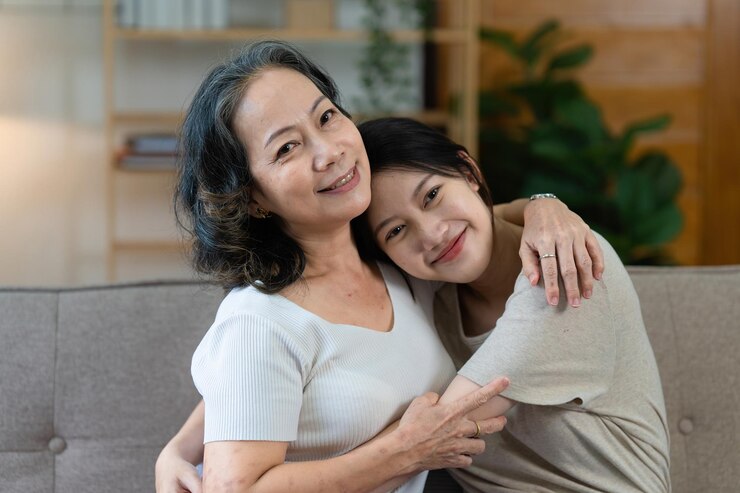 Photo 행복한 노인 아시아 여성과 그녀의 성인 딸이 소파에 껴안고 있다