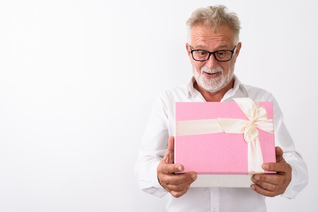 Uomo barbuto senior felice che sorride mentre guarda scioccato mentre apre la confezione regalo con gli occhiali su bianco