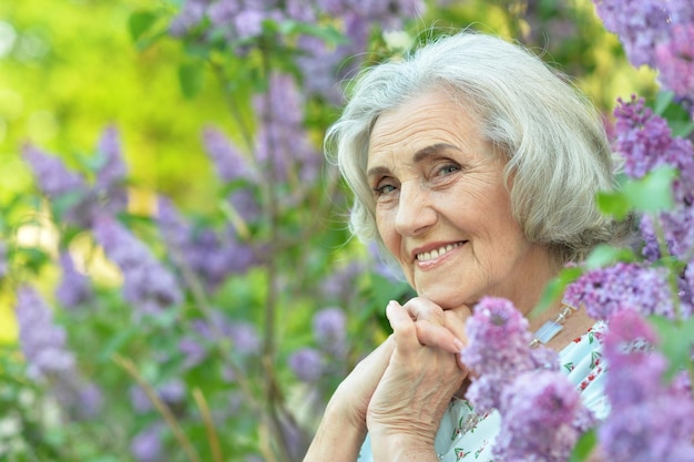 Happy senior beautiful woman on lilacs background in spring park