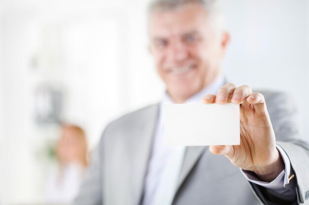 Photo happy senior businessman holding blank business card in the office. looking at camera. selective focus. focus on business card.