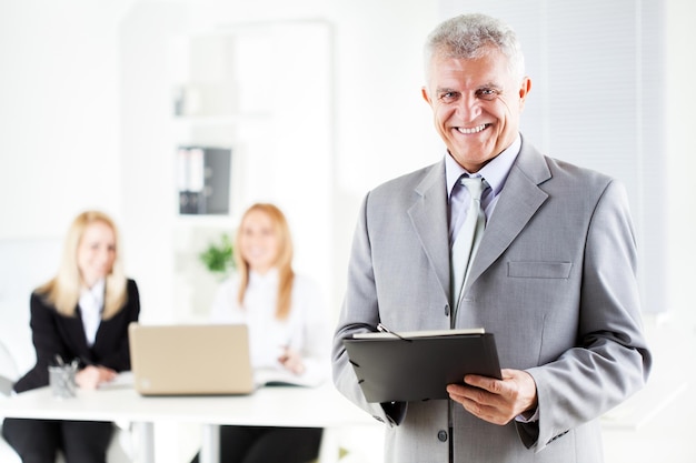 Happy senior businessman with documents standing in the office. Looking at camera. Selective Focus.