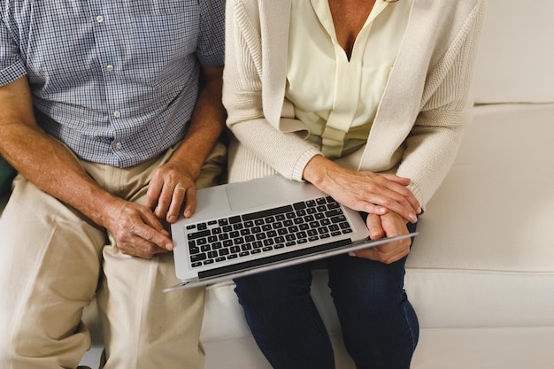 Happy senior caucasian couple in living room, sitting on sofa, using laptop