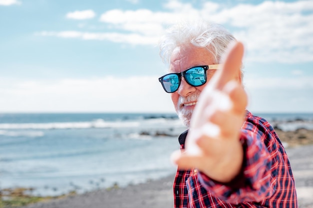 Счастливый пожилой кавказец смотрит в камеру, стоя на пляже в морском отпуске или на пенсии