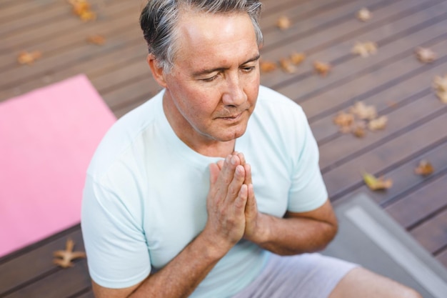 Happy senior caucasian man practicing yoga, meditating in sunny garden. healthy retirement lifestyle, spending time at home.