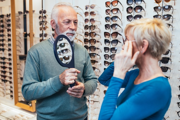 Happy senior couple choosing together eyeglasses frame in optical store.