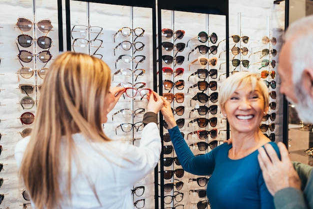 Happy senior couple choosing together eyeglasses frame in optical store.