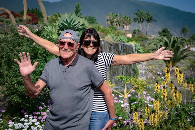 Happy senior couple in denim and sunglasses enjoying a sunny day in the garden looking at camera