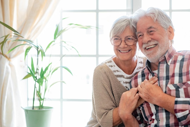 Happy senior couple embracing and laughing sitting at home expressing happiness and carefree