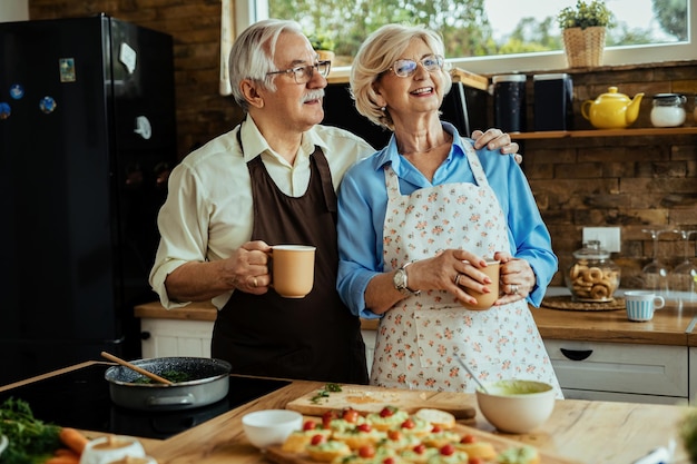 Happy senior couple enjoying in cup of coffee while cooking together in the kitchen