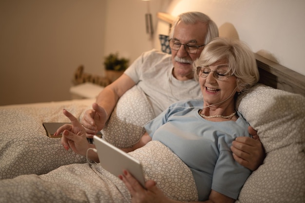 Happy senior couple enjoying in the evening while using digital tablet in bedroom