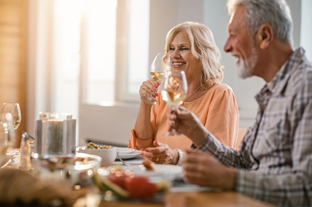 ダイニングテーブルでランチタイムにグラスワインを楽しんでいる幸せな年配のカップルフォーカスは女性にあります