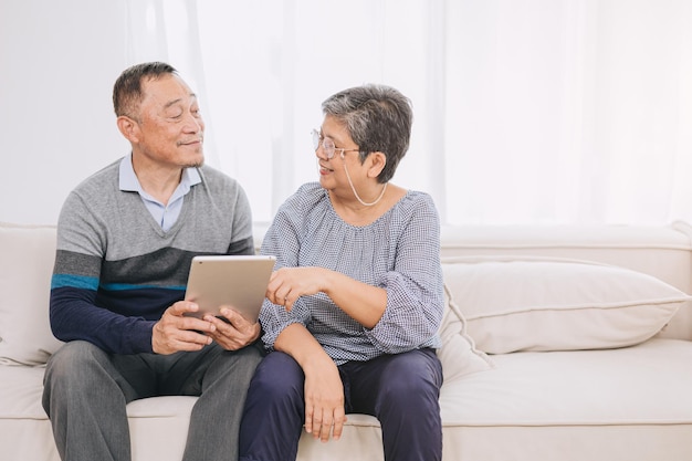 Happy senior couple enjoys technology together at home sofa Tablet for elderly couples Strengthen family bonds with modern technologyTech savvy husband and wife benefits of device for seniors