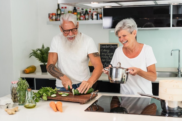 Happy senior couple having fun cooking together at home Main focus on man hands chopping cucumber