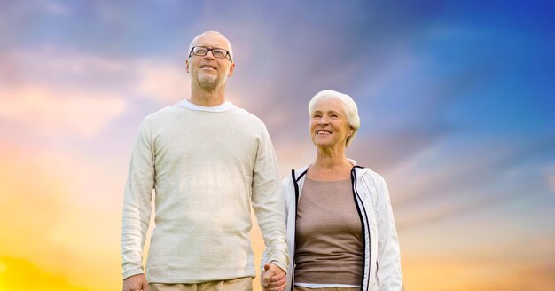 happy senior couple holding hands over evening sky