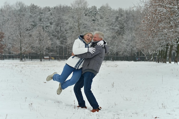 Felice coppia senior che si abbraccia al parco invernale innevato