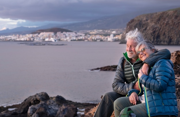 Фото Счастливая старшая пара обнимает друг друга, сидя на tcliff в зимний день, наслаждаясь на открытом воздухе