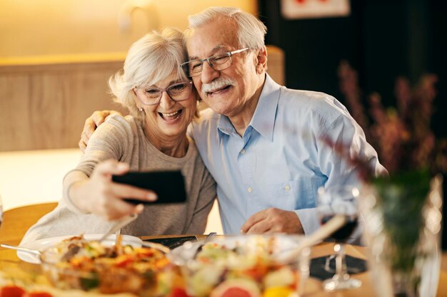 A happy senior couple is taking selfies on lunch table at home