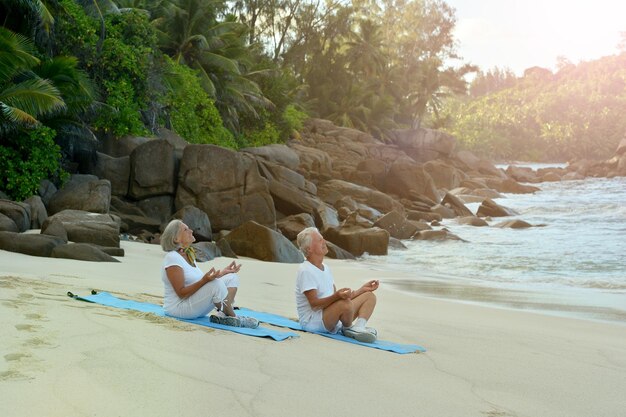 Happy Senior couple meditating in summer on seashore