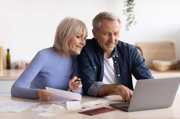 コンピューターを使用してオンラインで請求書を支払う幸せな年配のカップル
