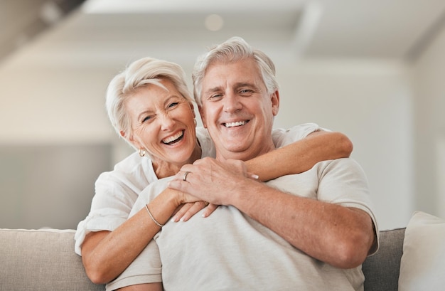 Happy senior couple portrait and hug on living room sofa for embrace relationship or love at home Mature woman hugging man with smile in happiness for care support or trust together in house