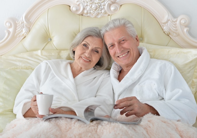 Felice coppia senior che legge a letto con una rivista