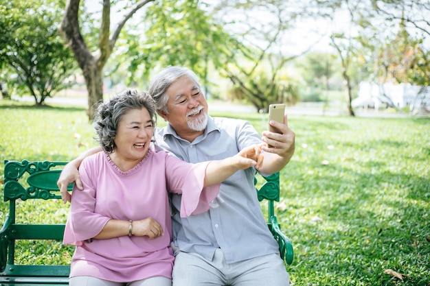 幸せな上級夫婦が公園でスマートフォンでセルフィーを撮っている