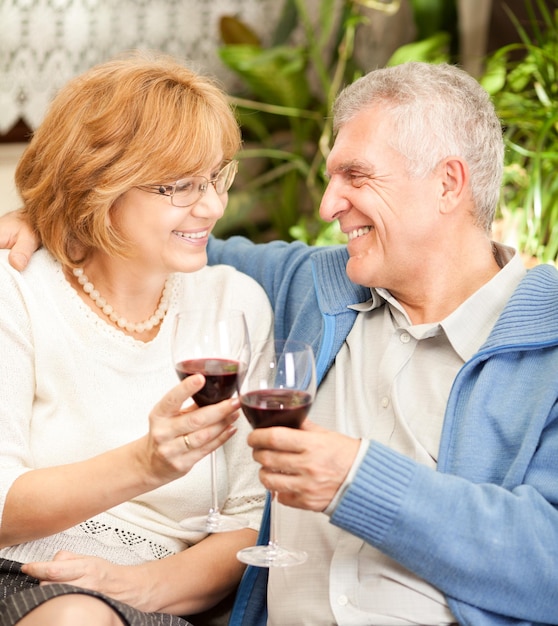 Happy senior couple toasting their anniversary with red wine at home ambient