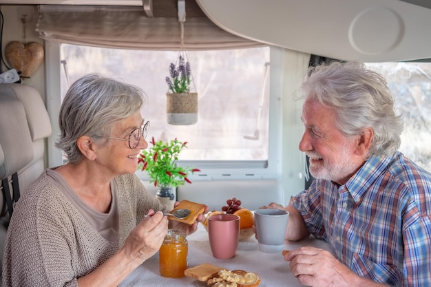 Happy senior couple in travel vacation leisure inside a camper\
van enjoying breakfast together